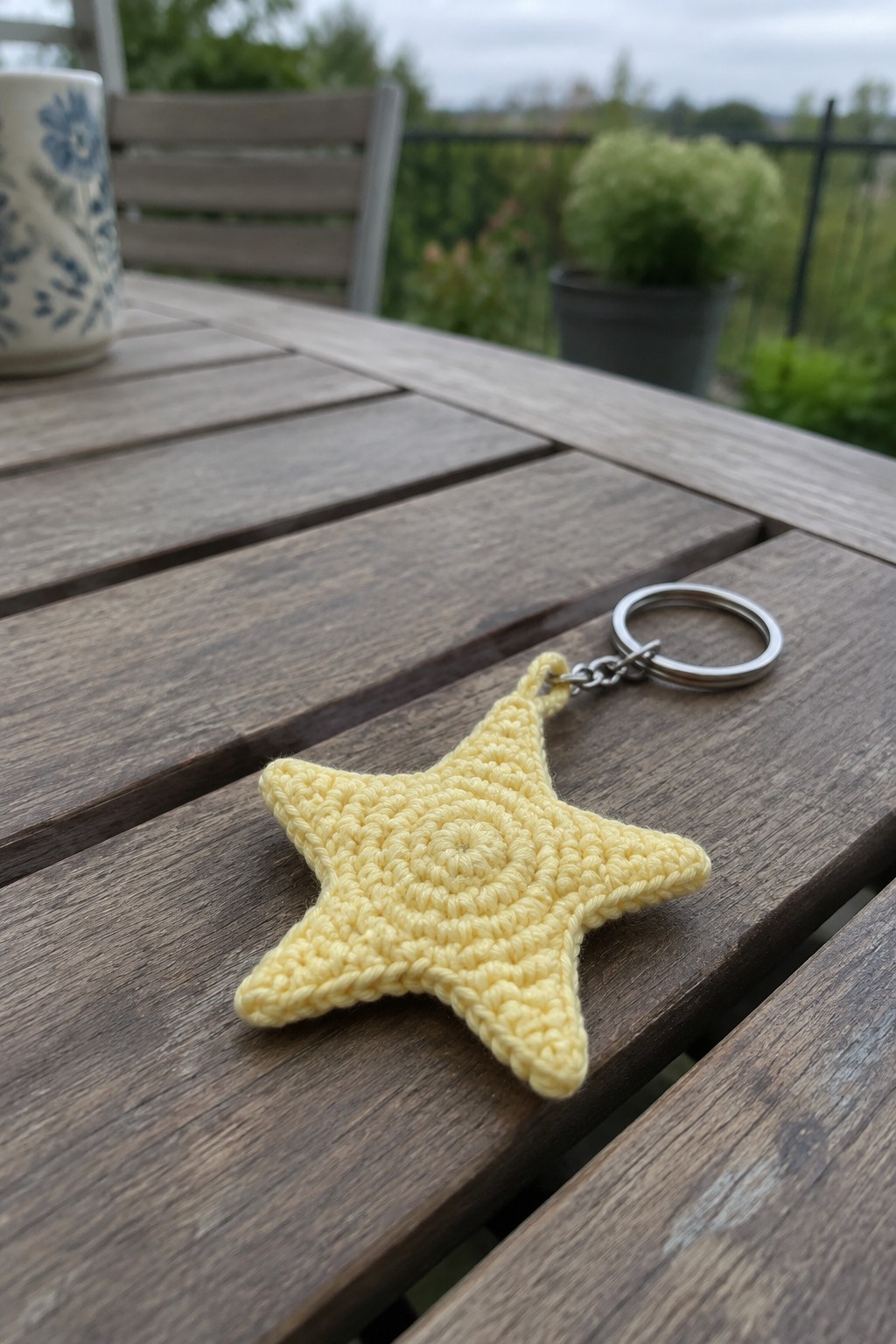 Yellow crocheted star keychain with metal ring on wooden outdoor table