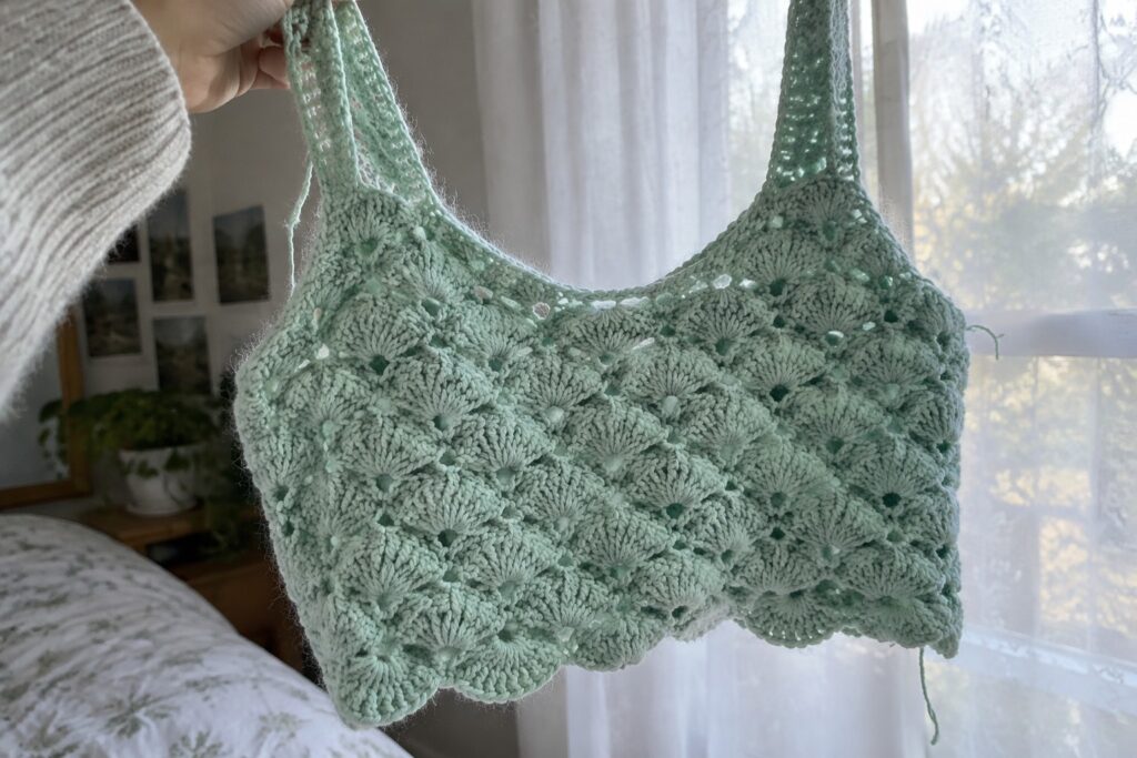 19 Free Crochet Top Patterns for Beginner-Friendly Projects Hand holding light green crocheted lace tank top in bedroom setting