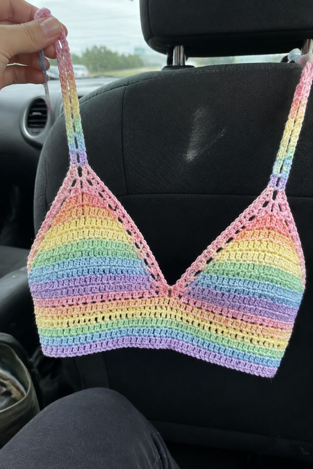 Crocheted pastel rainbow bikini top hanging from black car seat headrest.