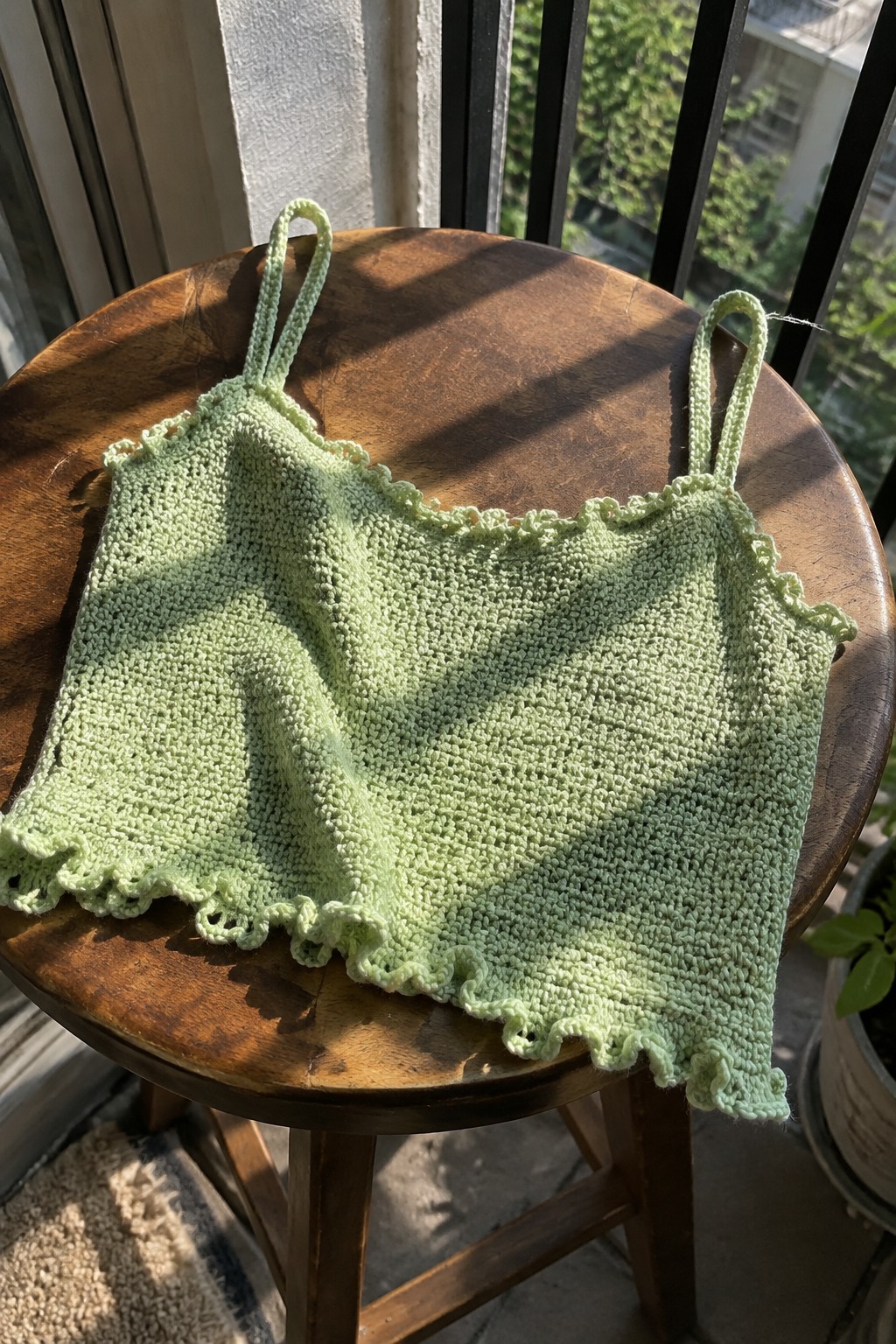 Light green knitted camisole with scalloped edges on sunlit wooden stool outdoors.