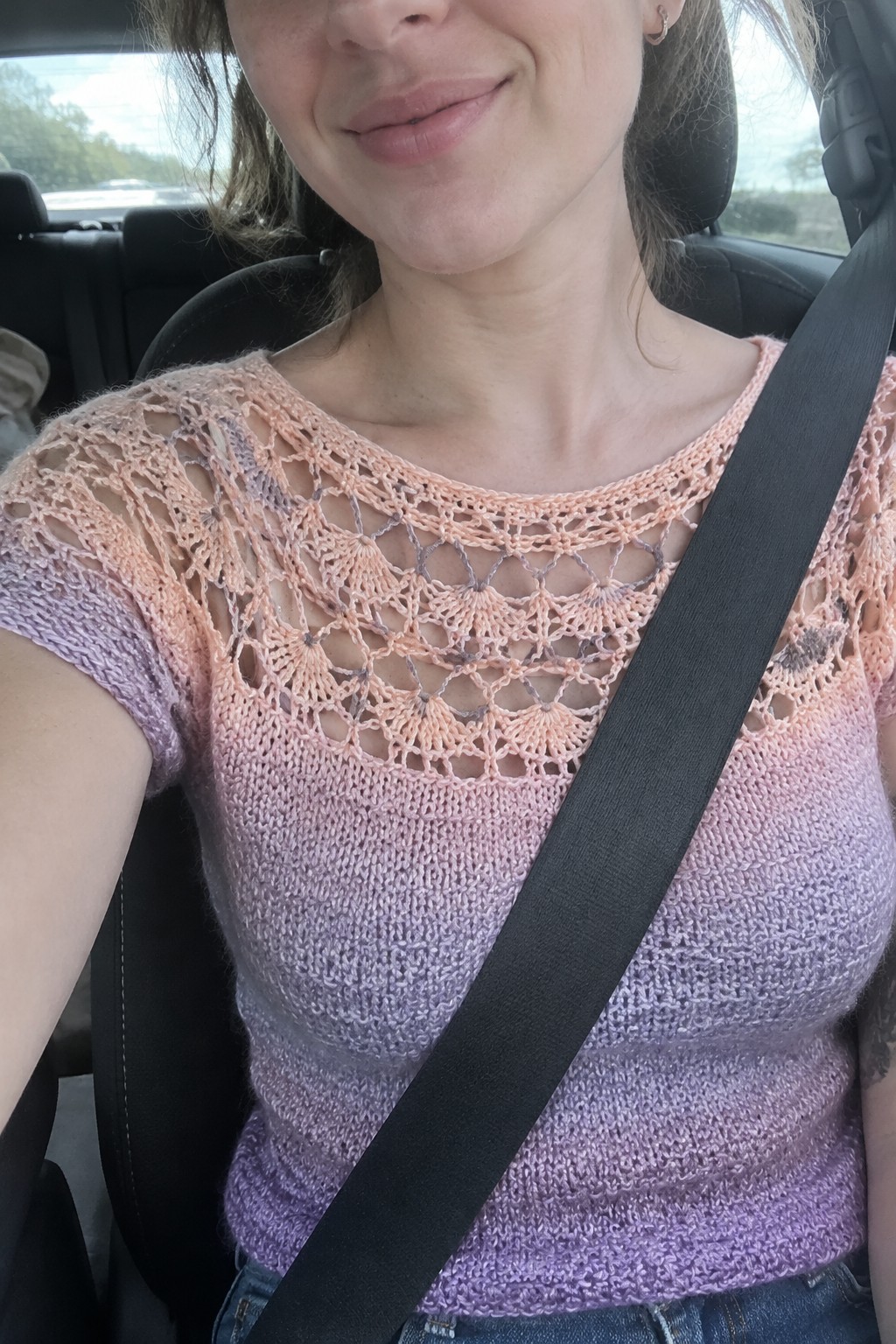 Woman in gradient pink-purple lace crochet top with black seatbelt in car