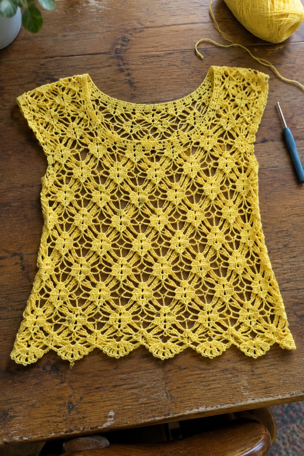 Yellow lace crochet top on wooden table with yarn and hook