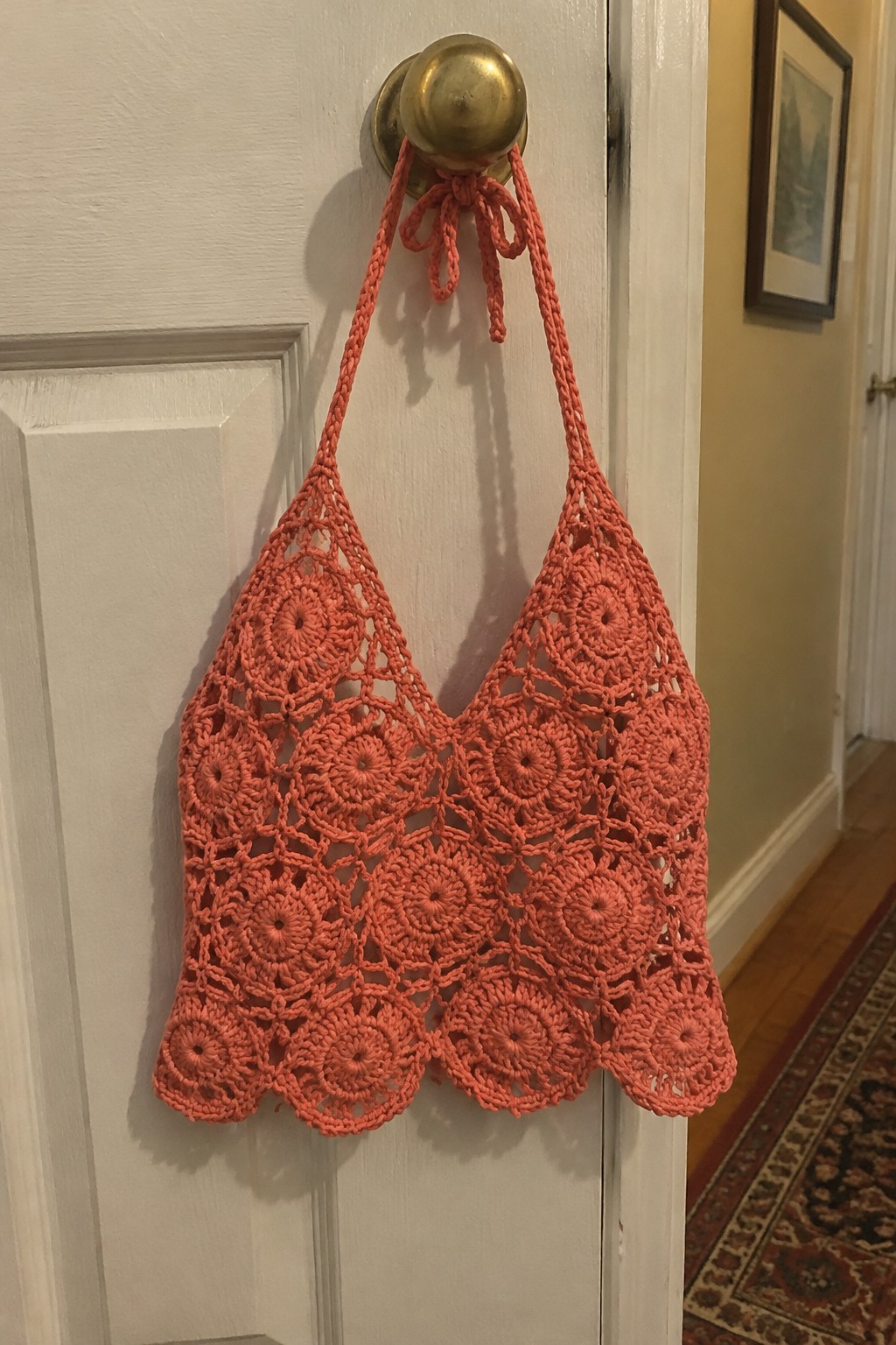 Coral crocheted lace bag hanging from brass knob on white door.
