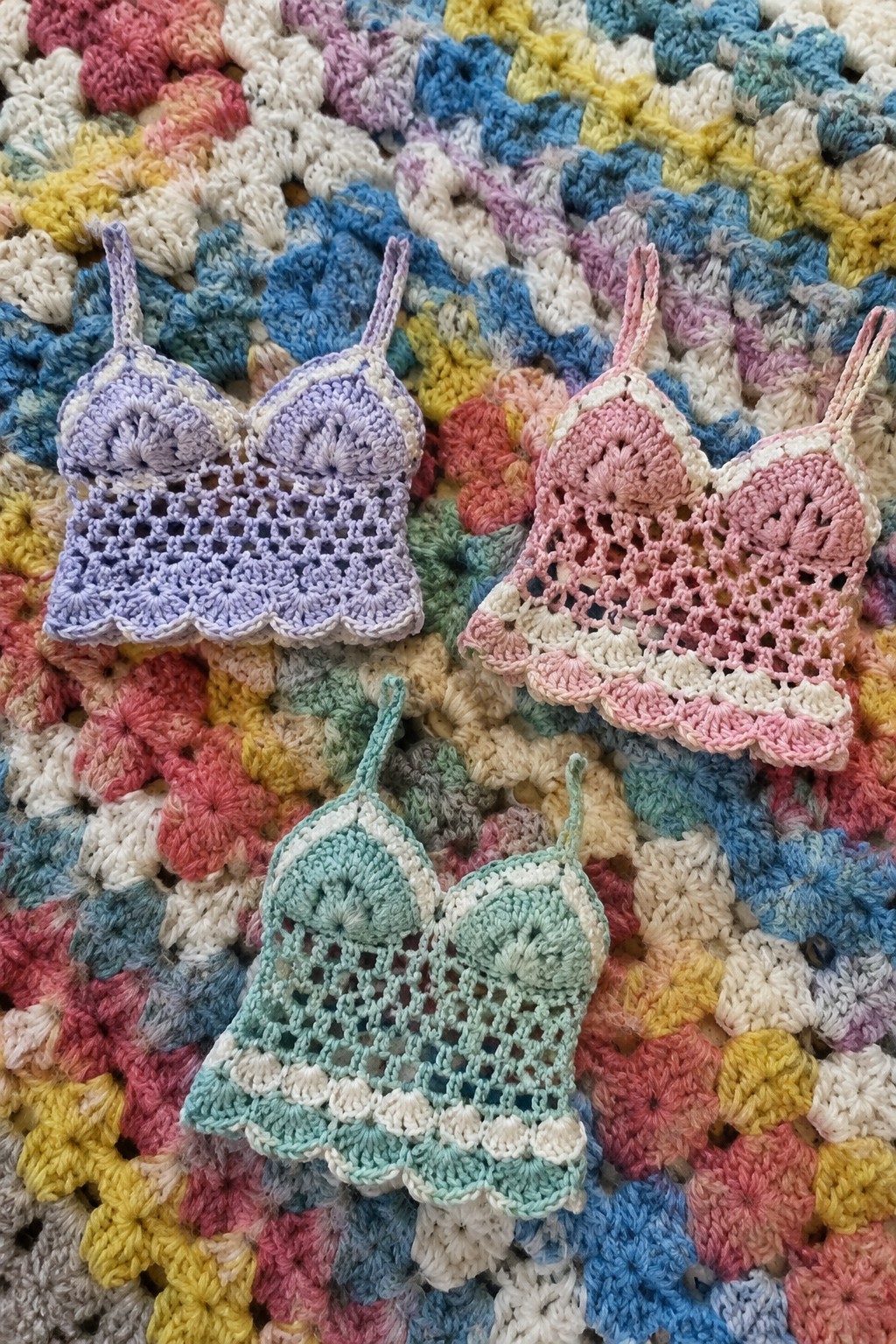 Three pastel crocheted bralettes on a vibrant granny square blanket.