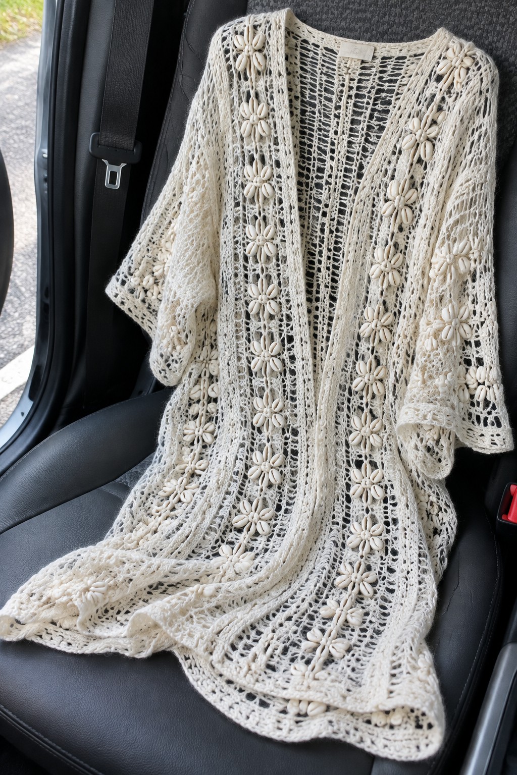 Cream lace cardigan with floral shell patterns on black car seat