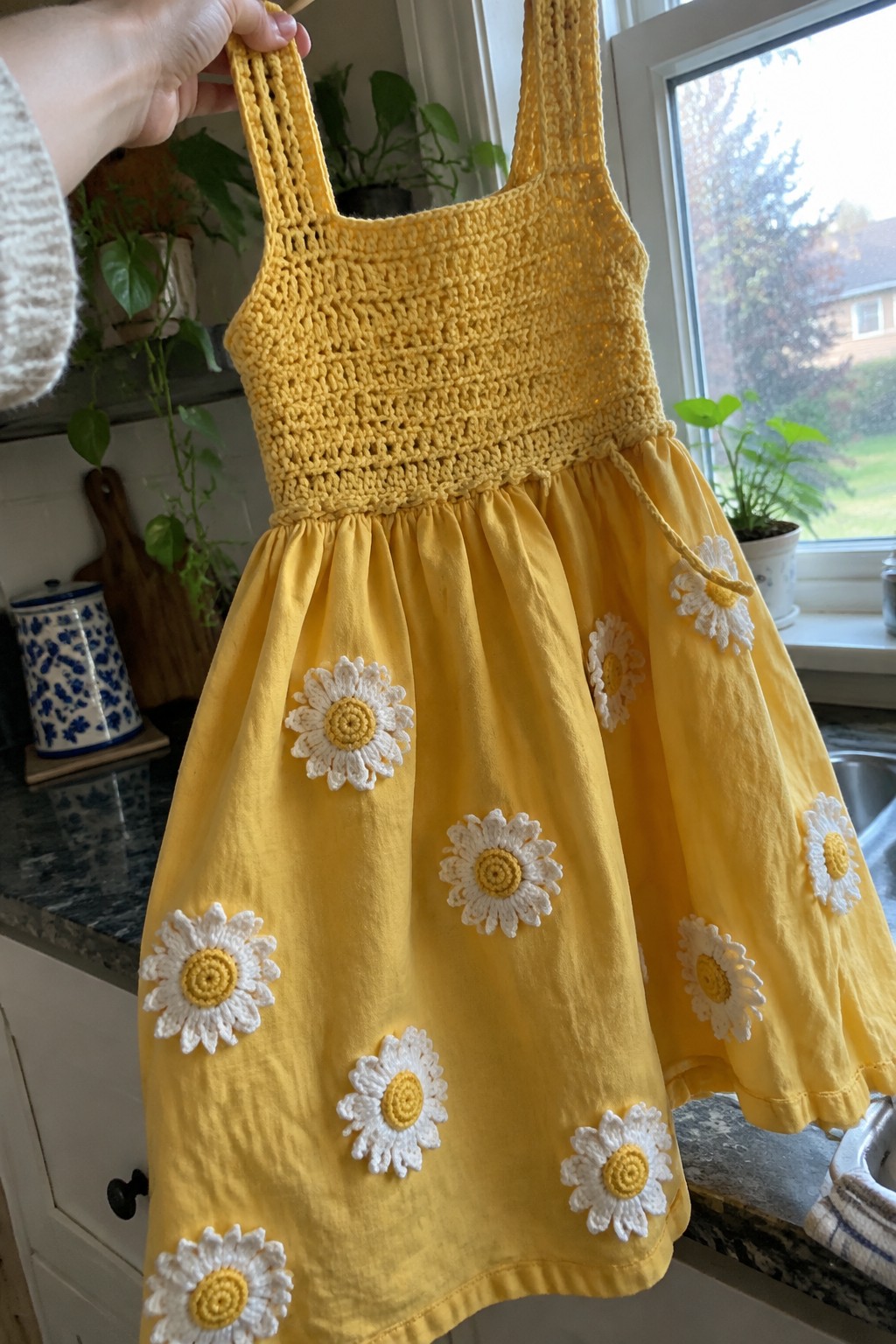 Yellow crocheted sundress with daisy appliques held up in a kitchen.