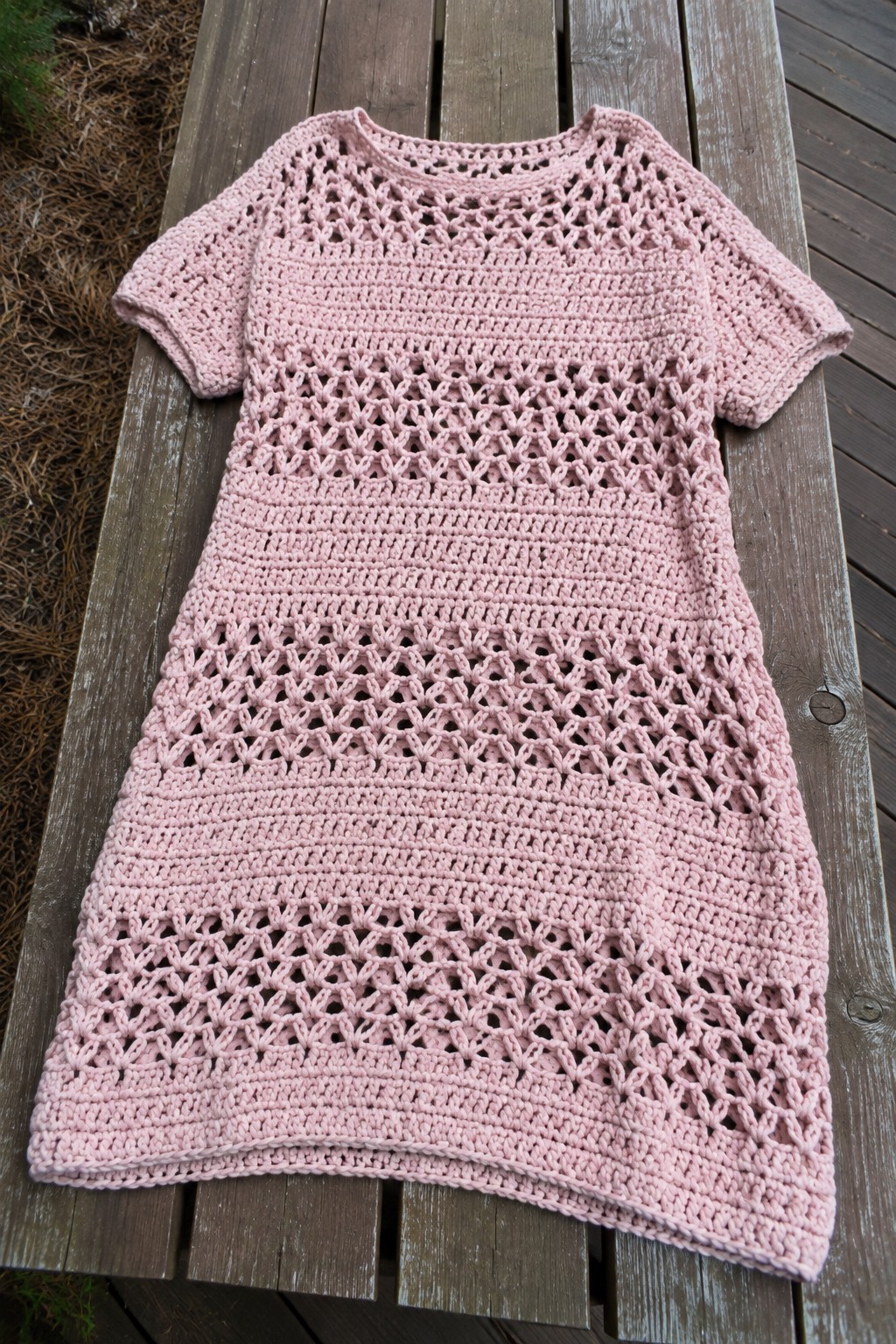 Pink crocheted lace dress laid flat on wooden outdoor bench