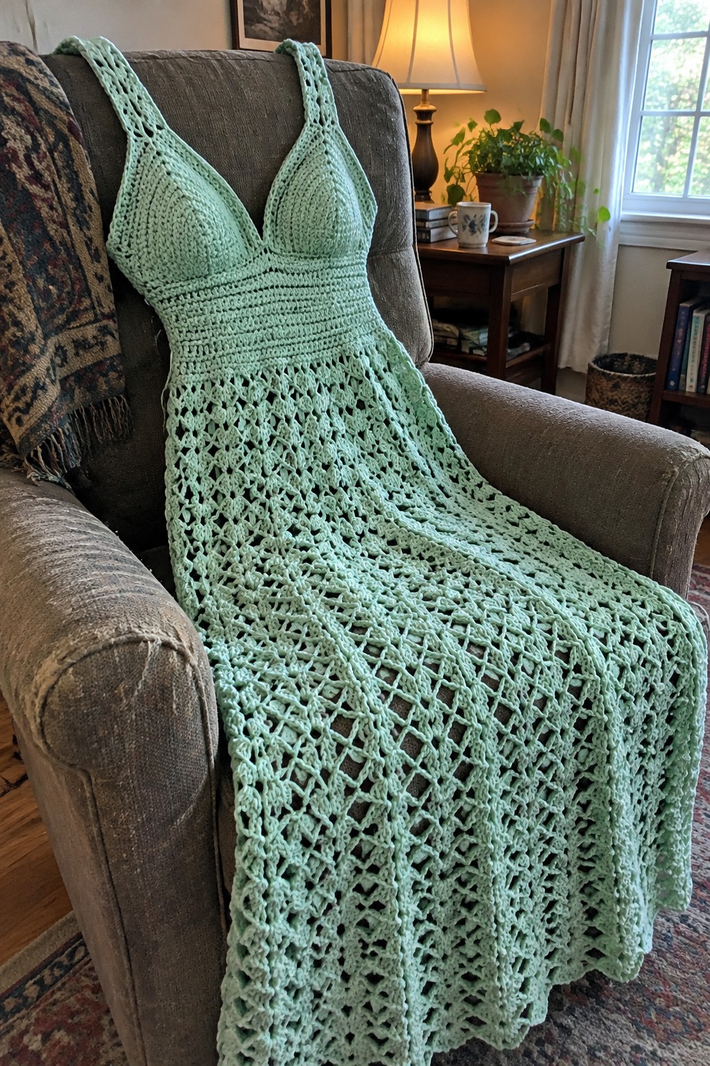 A light green crocheted dress with a fitted bodice and long openwork skirt draped over a gray armchair.
