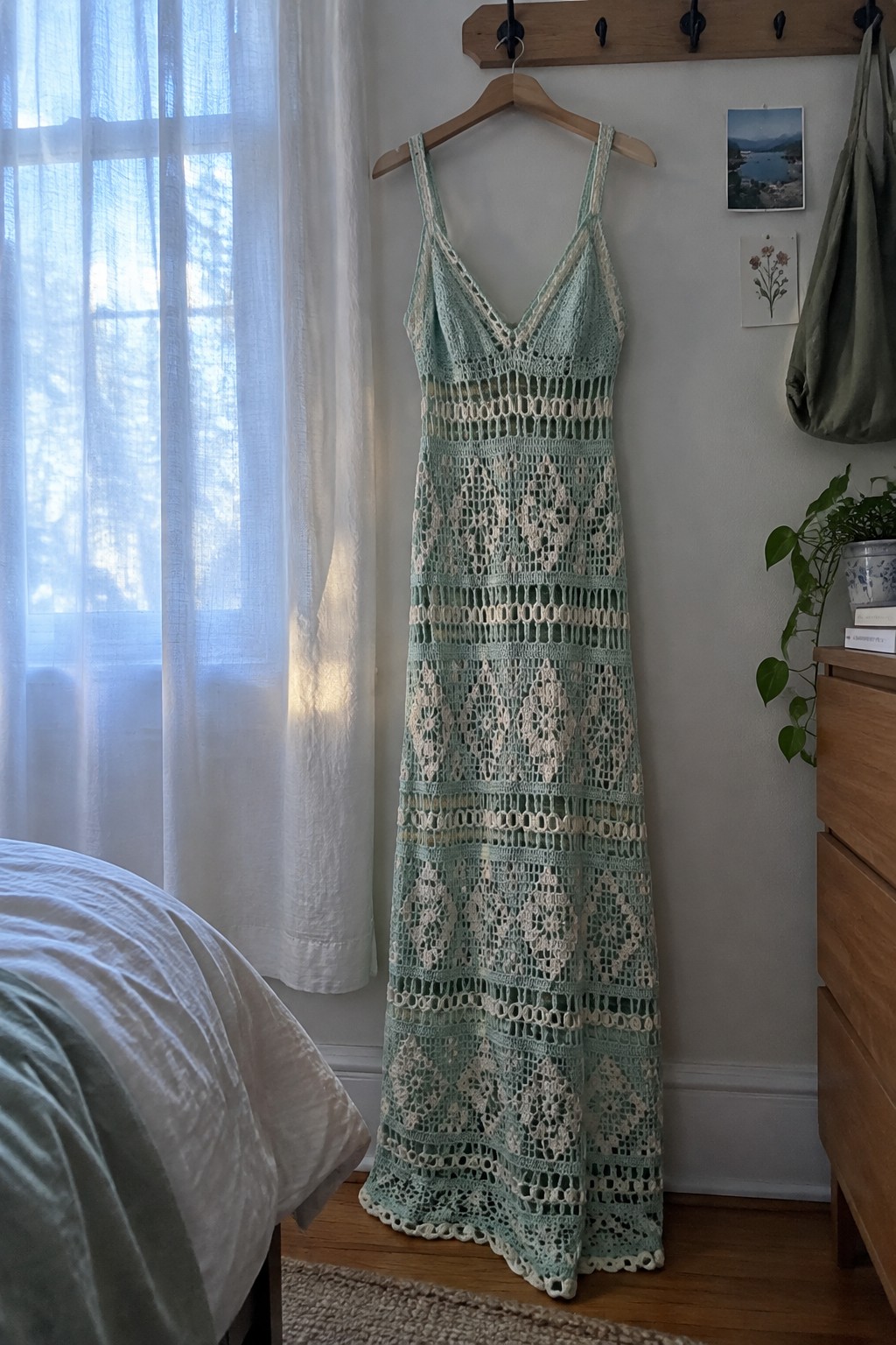 Mint green and white crocheted lace maxi dress hanging on wooden hanger in bedroom