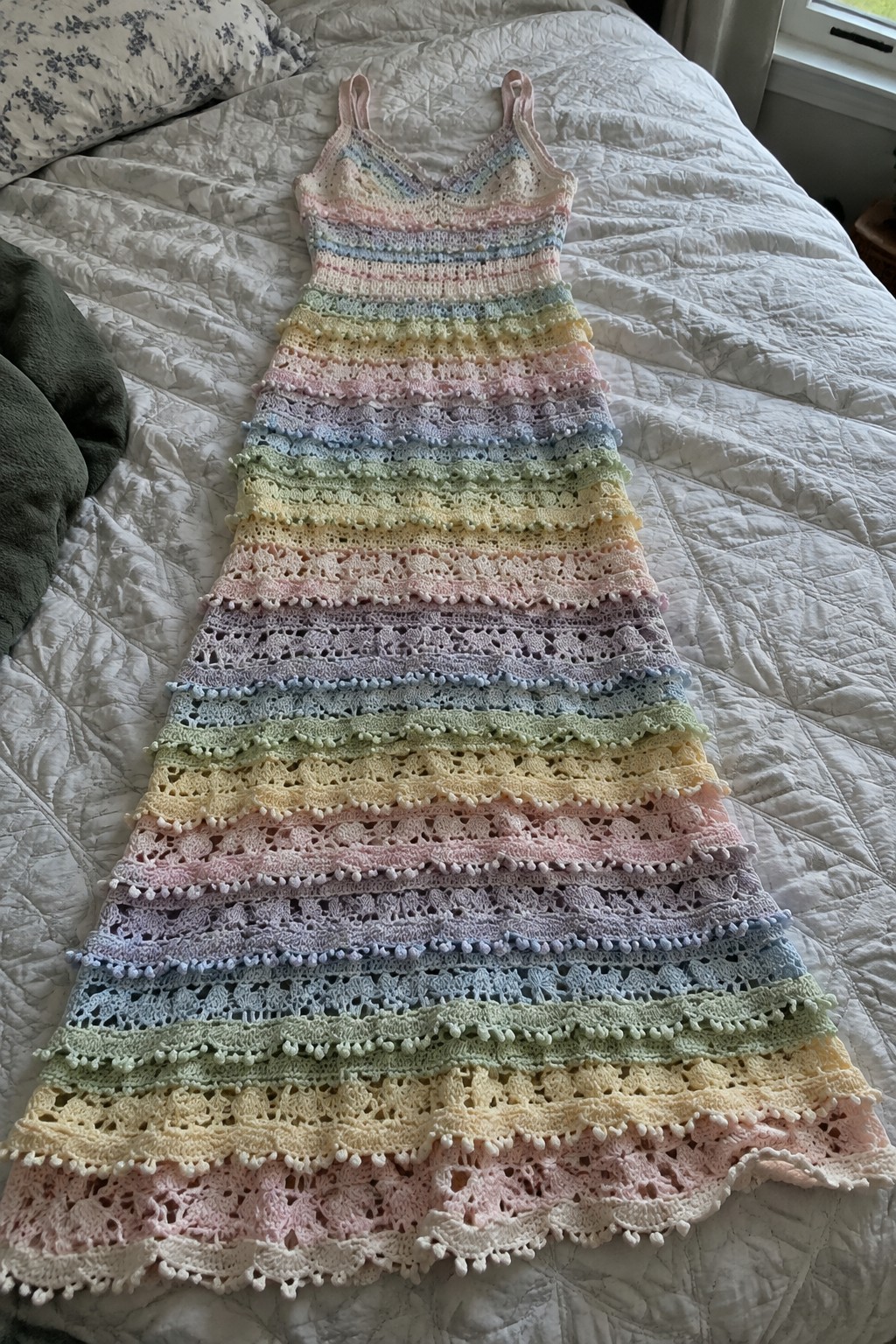 Pastel rainbow crocheted maxi dress with lace patterns on white quilted bed