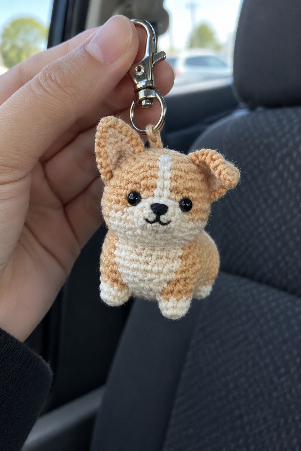 Hand holding crocheted tan corgi keychain with metal clasp inside car