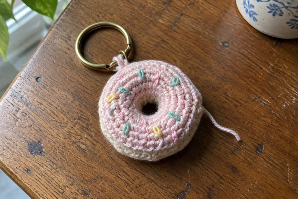 21 Pastel Crochet Keychain Ideas Featuring Coordinated Color Palettes Crocheted pink donut keychain with pastel sprinkles and brass ring on wooden table