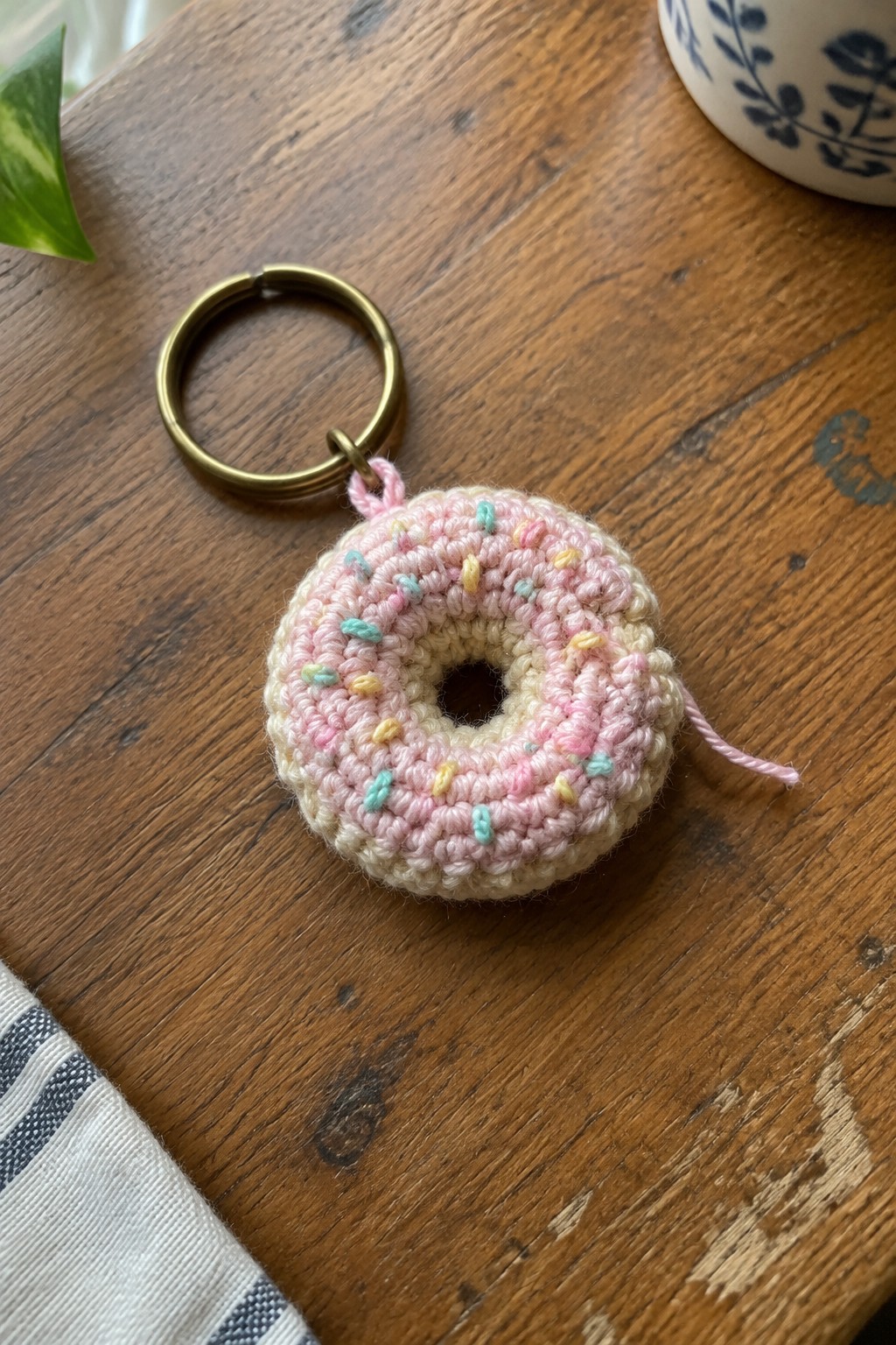 Crocheted pink donut keychain with pastel sprinkles and brass ring on wooden table