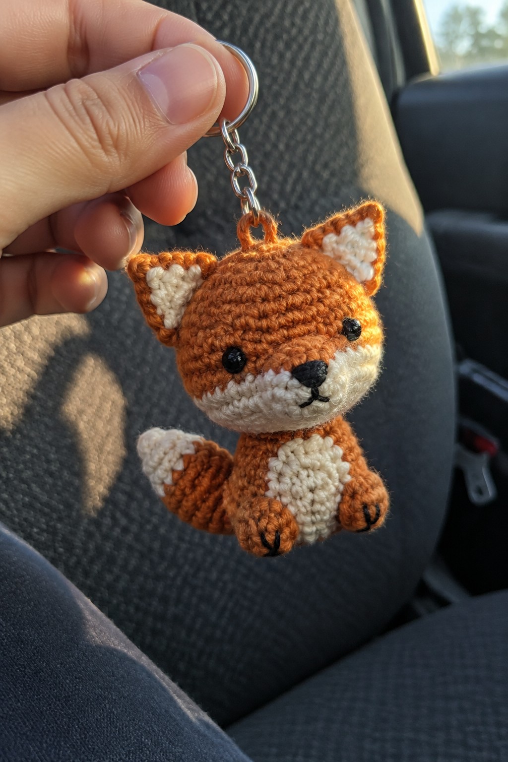 Hand holding crocheted orange fox keychain with white accents and metal ring