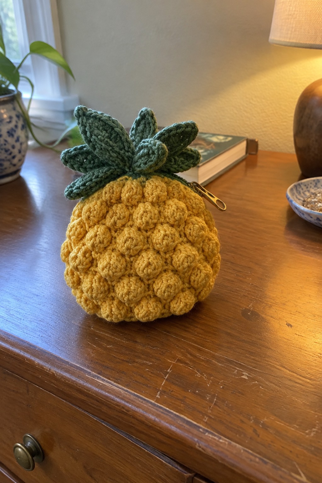 Yellow crocheted pineapple pouch with green leaves and zipper on wooden table