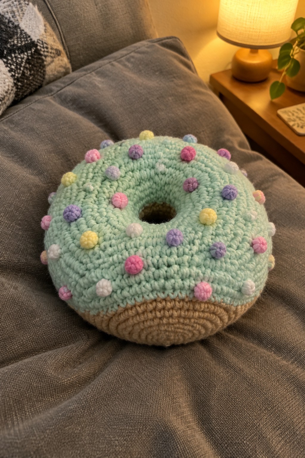 Mint green crocheted donut pillow with colorful sprinkles on gray couch