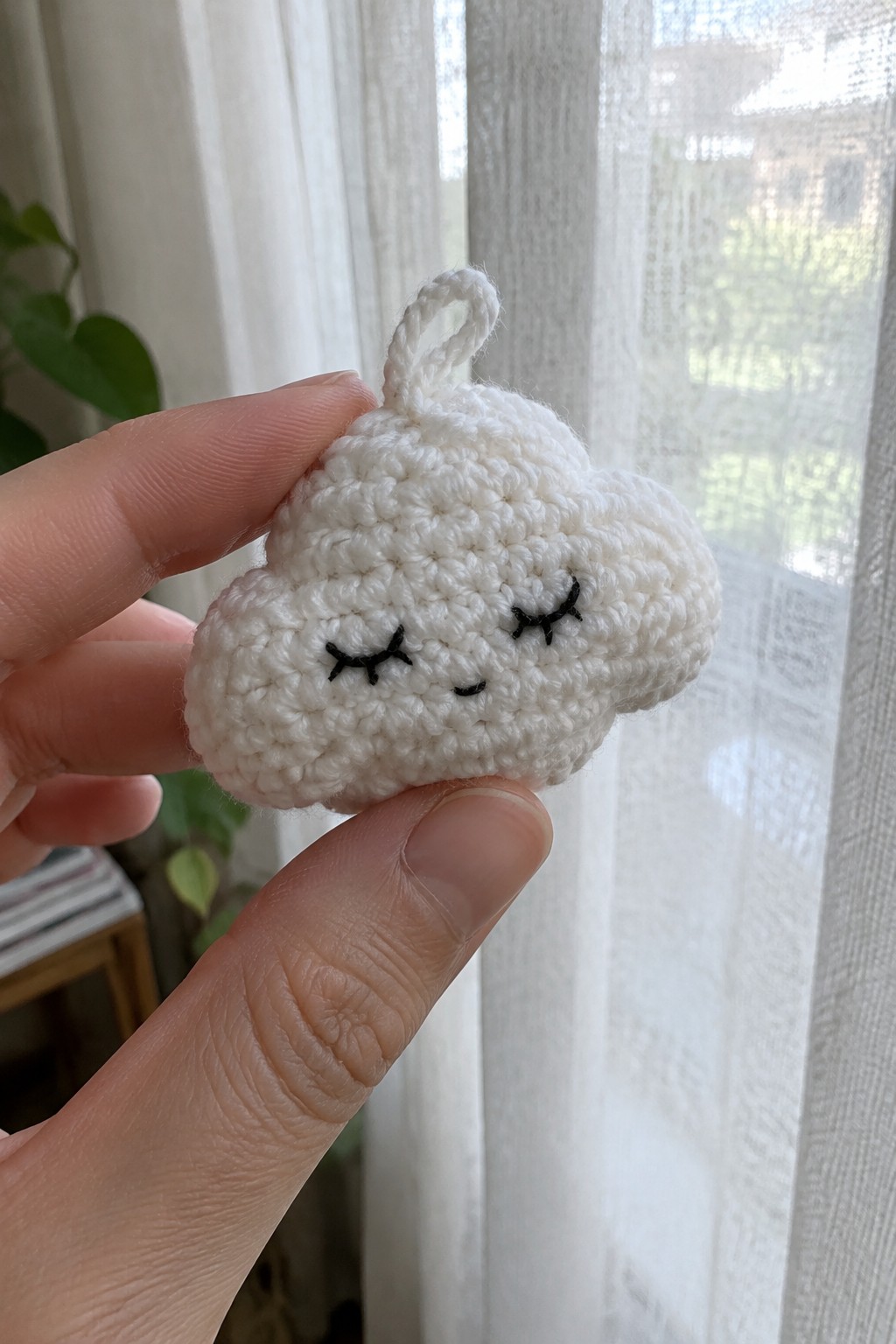 Hand holding small white crocheted cloud with closed black eyes and top loop