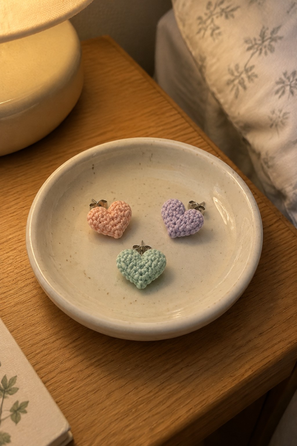 Three pastel crocheted heart earrings in a speckled white ceramic bowl on wood