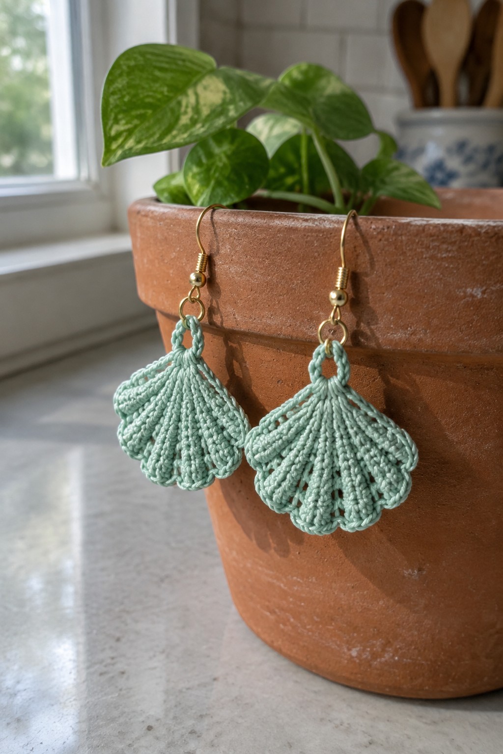 Mint green crocheted shell earrings dangling from terracotta plant pot rim