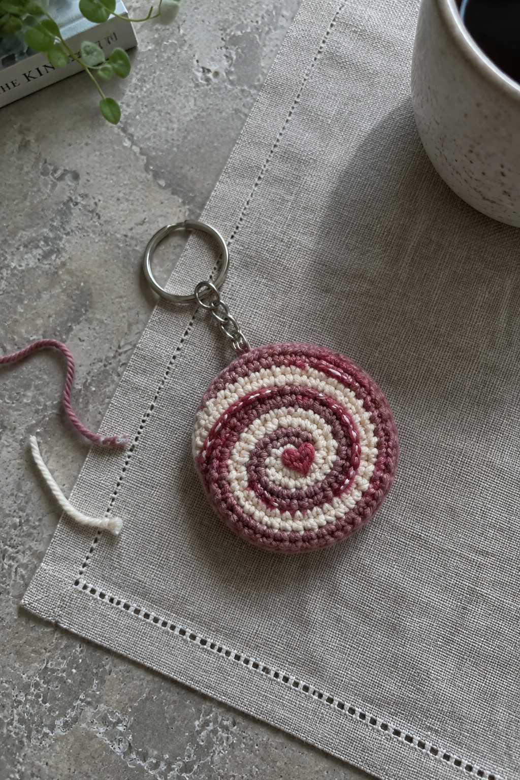 Pink crocheted keychain with spiral rings and heart on beige linen