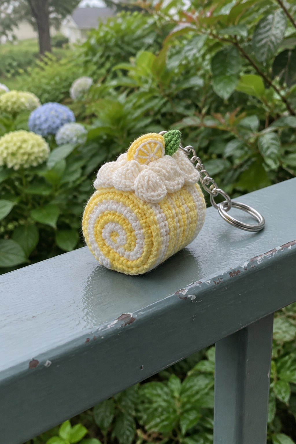 Yellow and white crocheted lemon roll keychain on green wooden railing outdoors