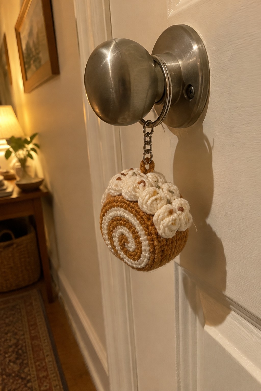 Crocheted cinnamon roll keychain dangling from silver door knob on white door