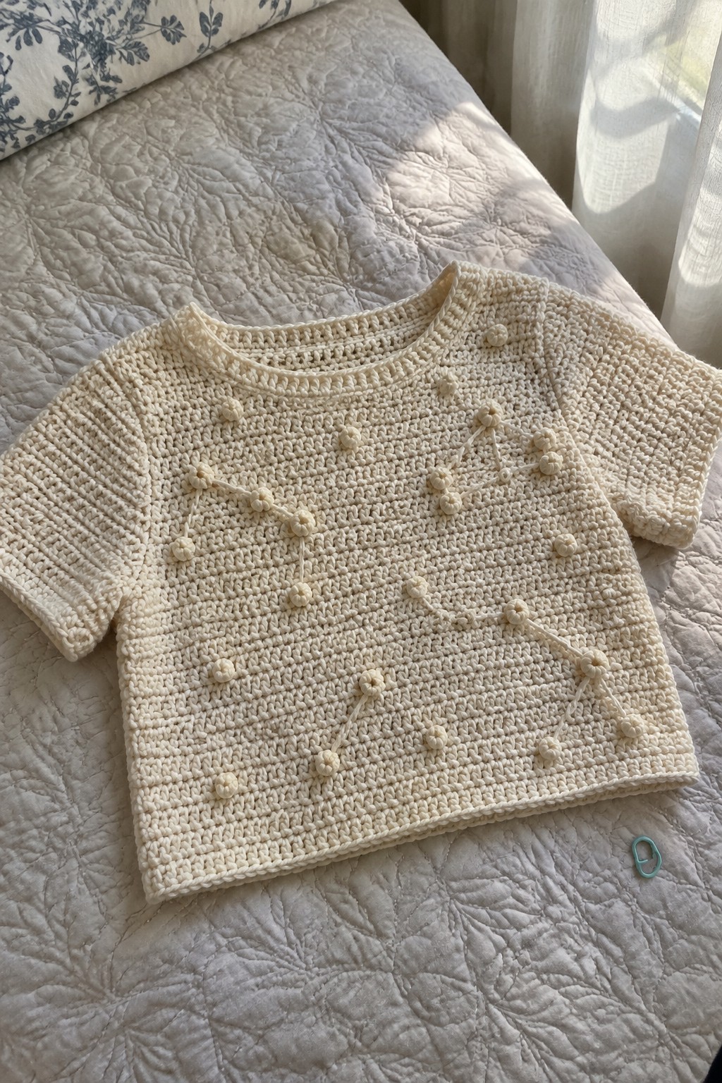 Cream crocheted short-sleeve top with bobble pattern on quilted bed