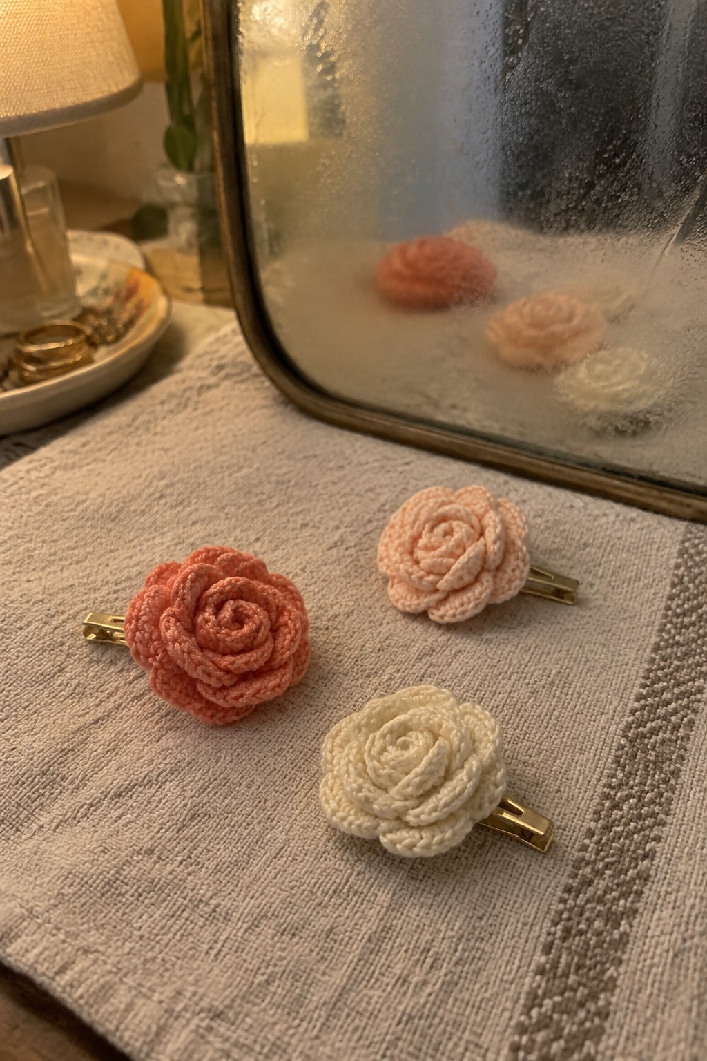 Three crocheted rose hair clips in peach and cream on a beige towel