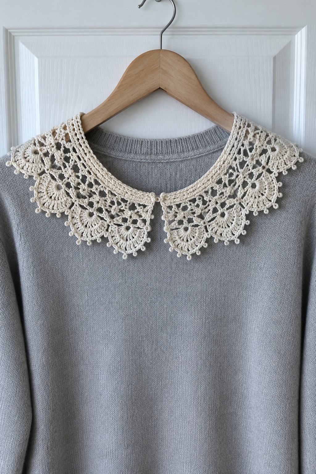Gray sweater with a cream crocheted lace collar on a wooden hanger.