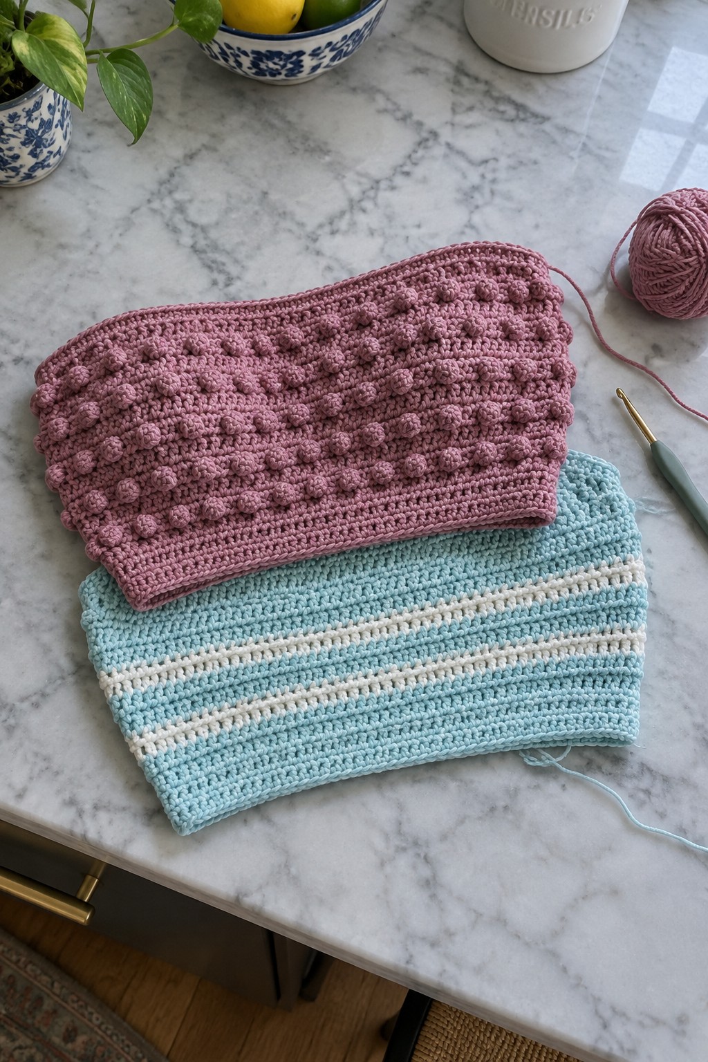 Pink bobble and blue striped crochet headbands with yarn on marble counter