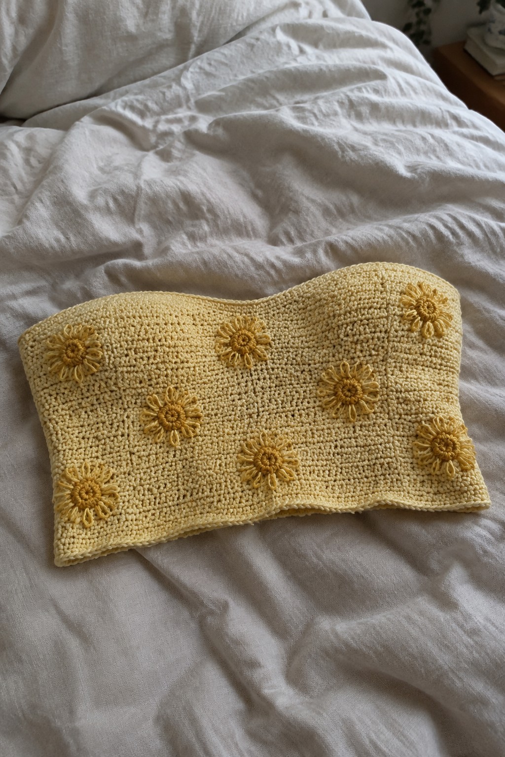 Yellow crocheted bandeau top with sunflower appliqués on white bedsheets