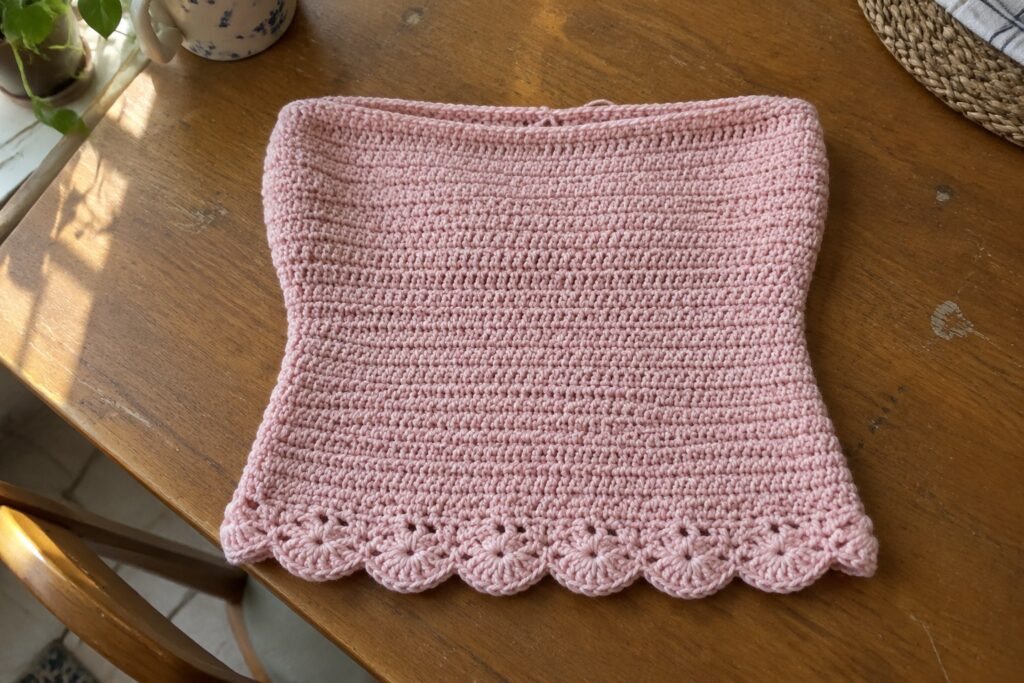 Pink crocheted scarf with scalloped lace border on wooden table