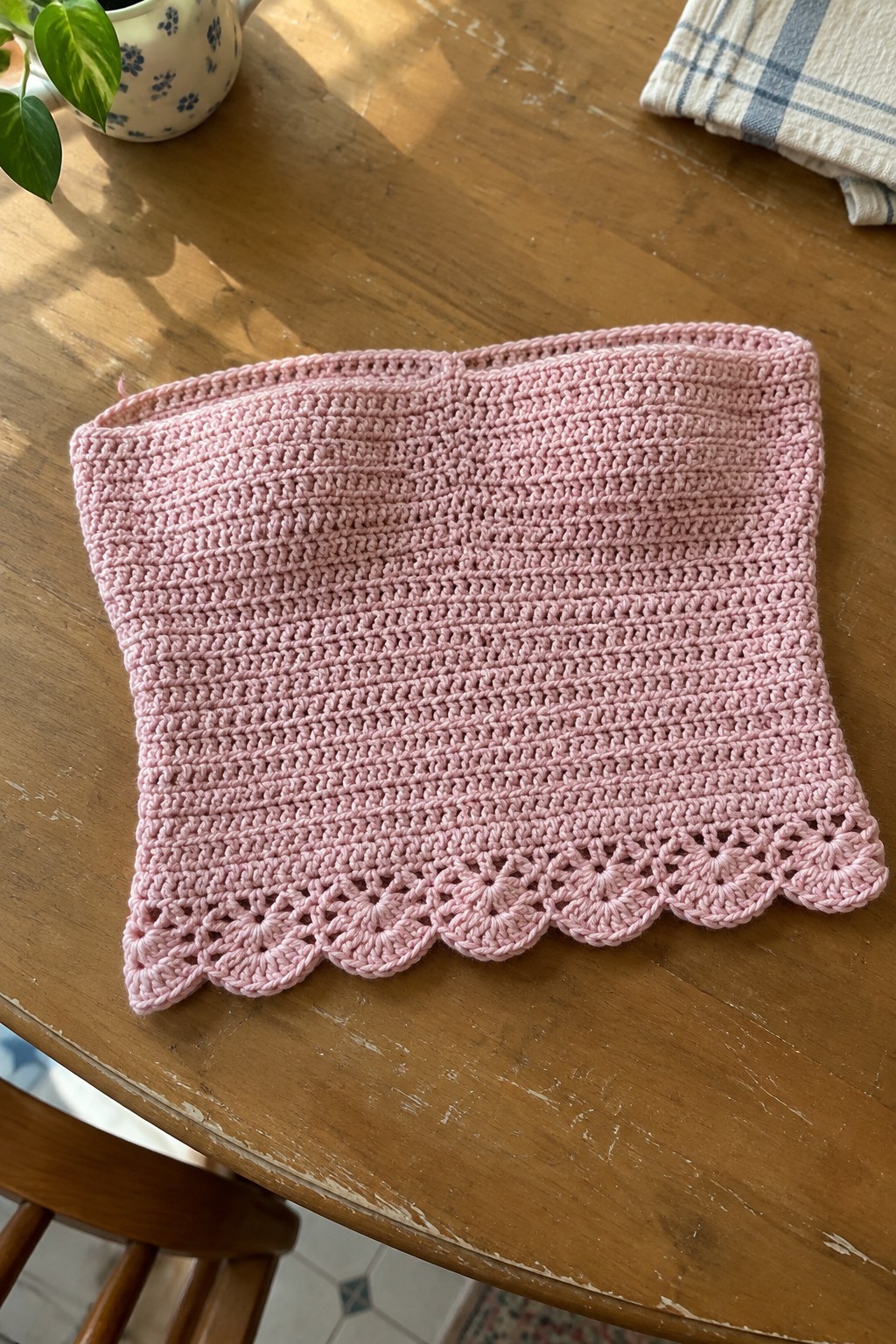 Pink crocheted scarf with scalloped lace border on wooden table