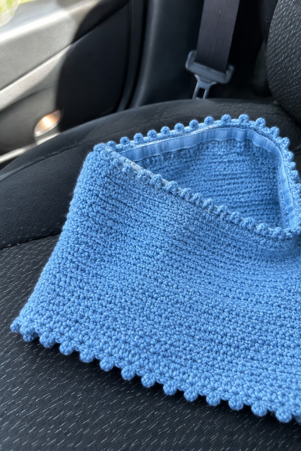 Blue crocheted bib with scalloped bobble trim on black car seat