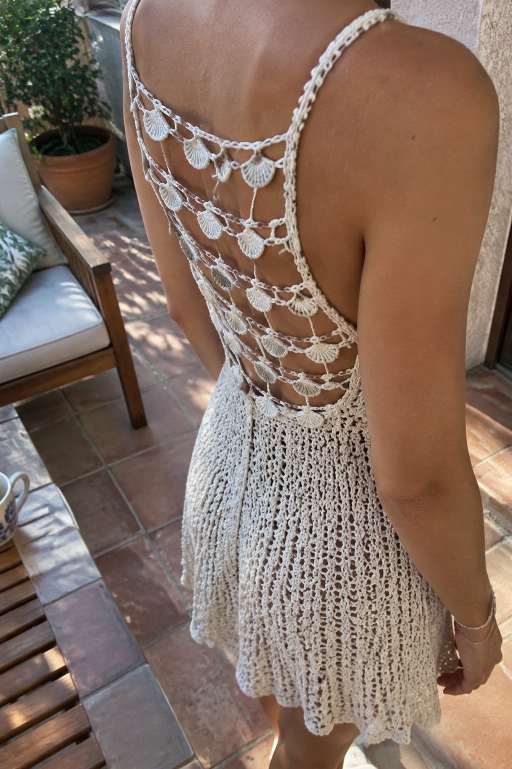 Woman in white open-back crochet dress with seashell details on patio