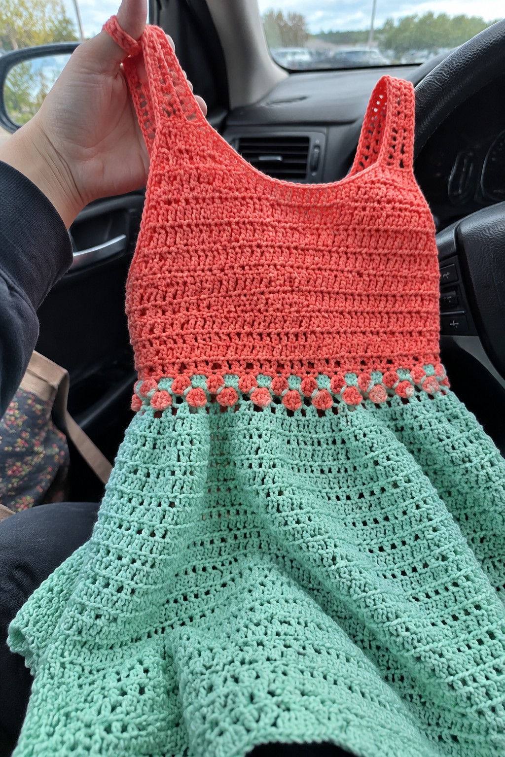 Crocheted dress with coral bodice and mint green lace skirt held up in a car.