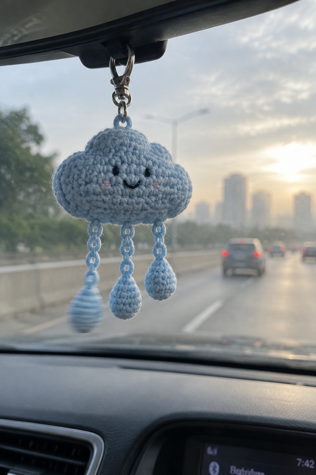 Light blue crocheted cloud charm with smiling face and raindrops hangs from car mirror