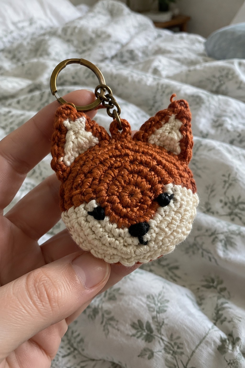Hand holding crocheted orange fox keychain with white muzzle and brass ring.