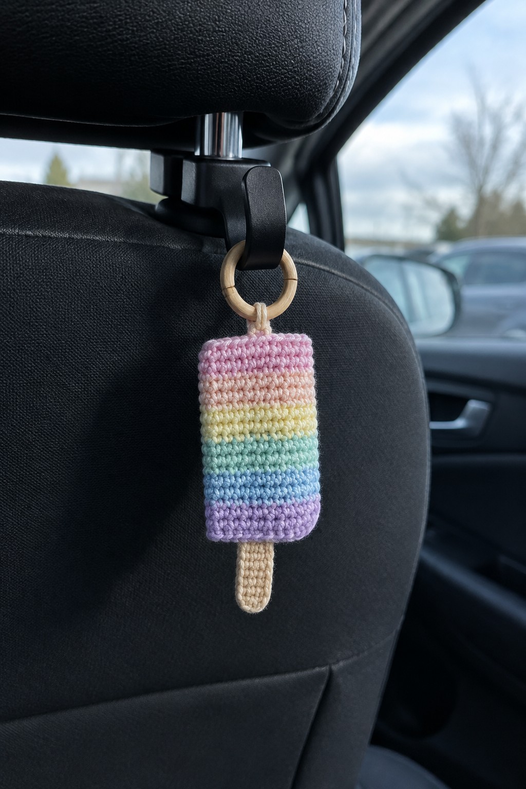 Rainbow crocheted popsicle hanging from wooden ring on car seat headrest.