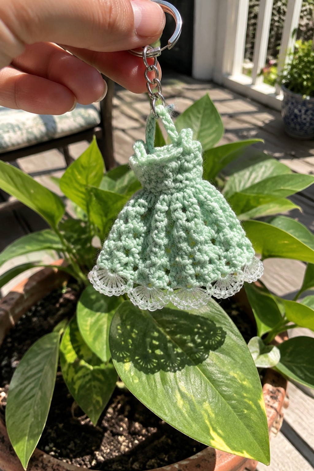 Hand holding mint green crocheted dress keychain with white lace trim.