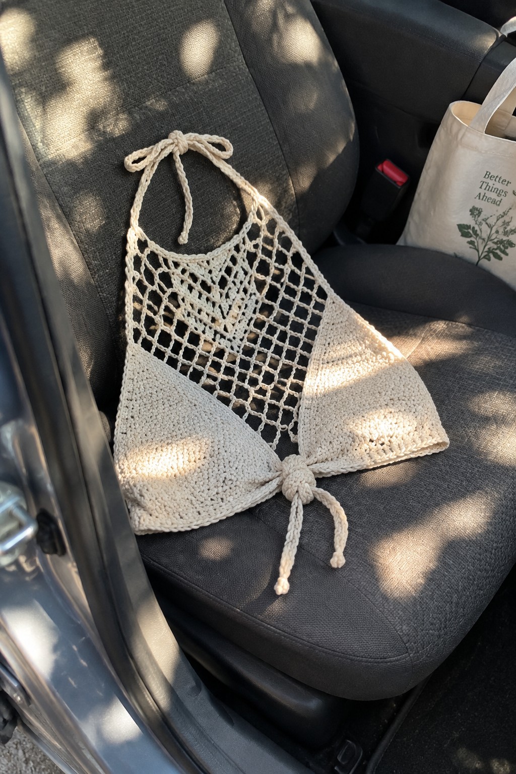 Crocheted halter top with mesh upper section and tied solid cups on a car seat.