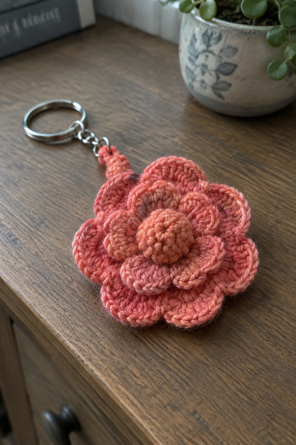 Coral crocheted flower keychain with silver ring on wooden table near plant