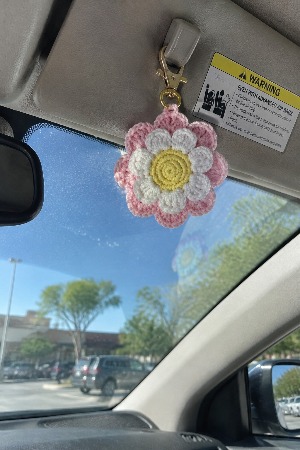 Pink and white crocheted daisy keychain hanging from car sun visor