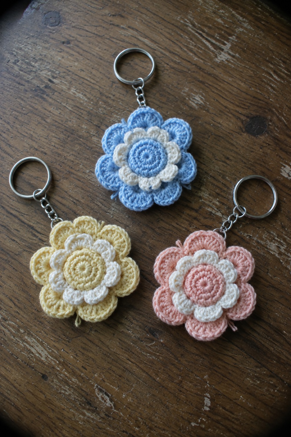 Three colorful crocheted flower keychains with rings on dark wood.