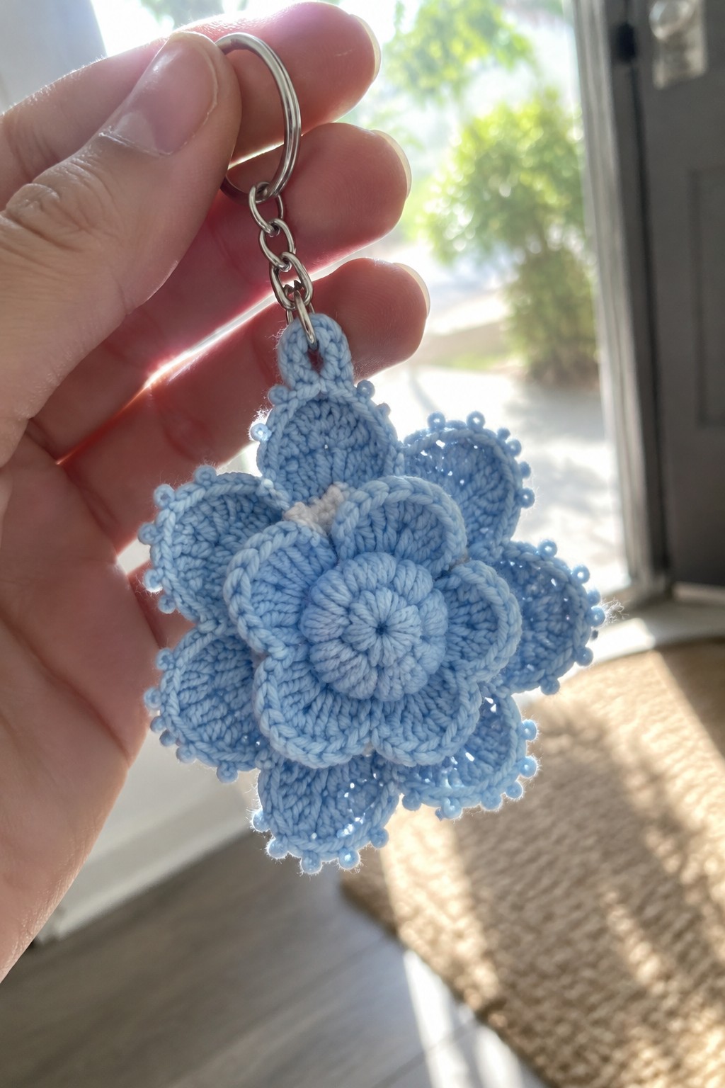 Hand holding light blue crocheted flower keychain with silver metal ring