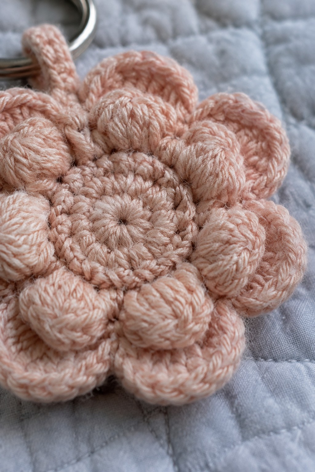 Peach crocheted flower keychain with metal ring on light blue quilted fabric.