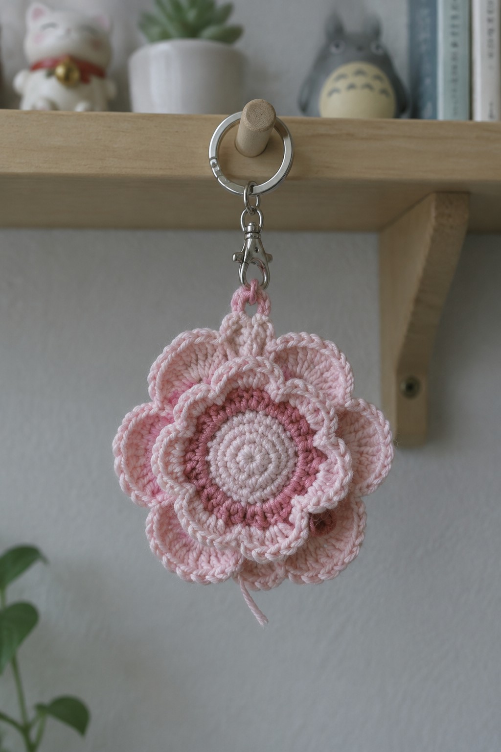 Pink crochet flower keychain hanging from wooden shelf with metal clasp