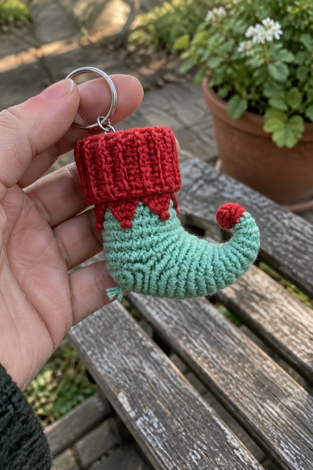 A small crocheted Christmas stocking keychain in red and mint green held in a hand.