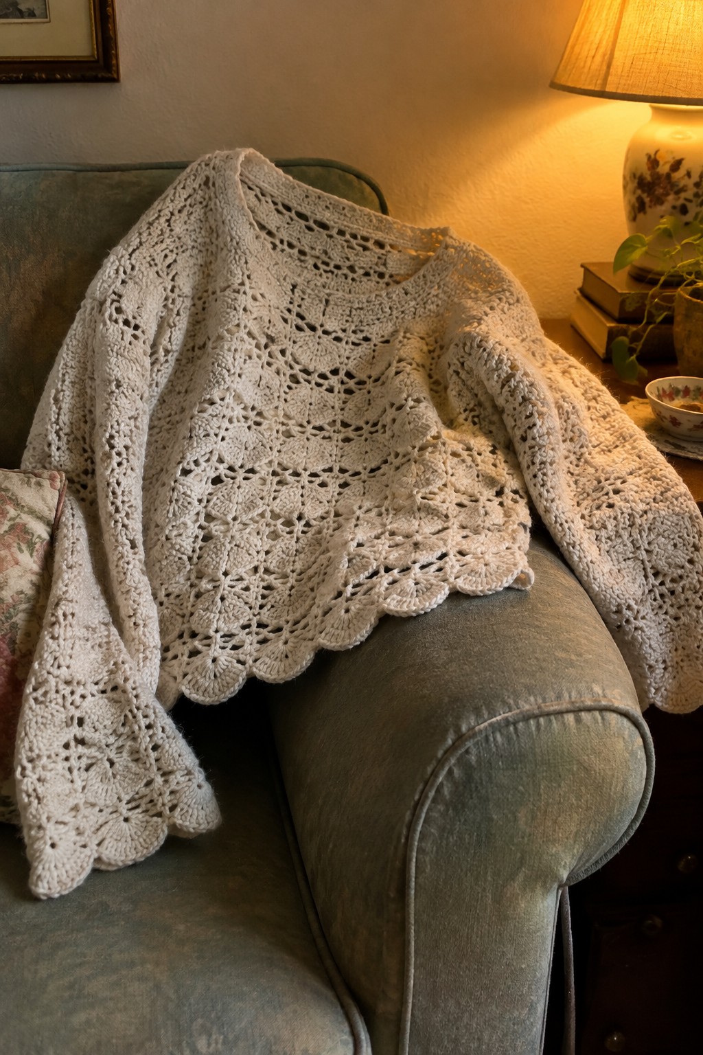 Cream crocheted lace sweater draped over a teal upholstered armchair beside a lamp