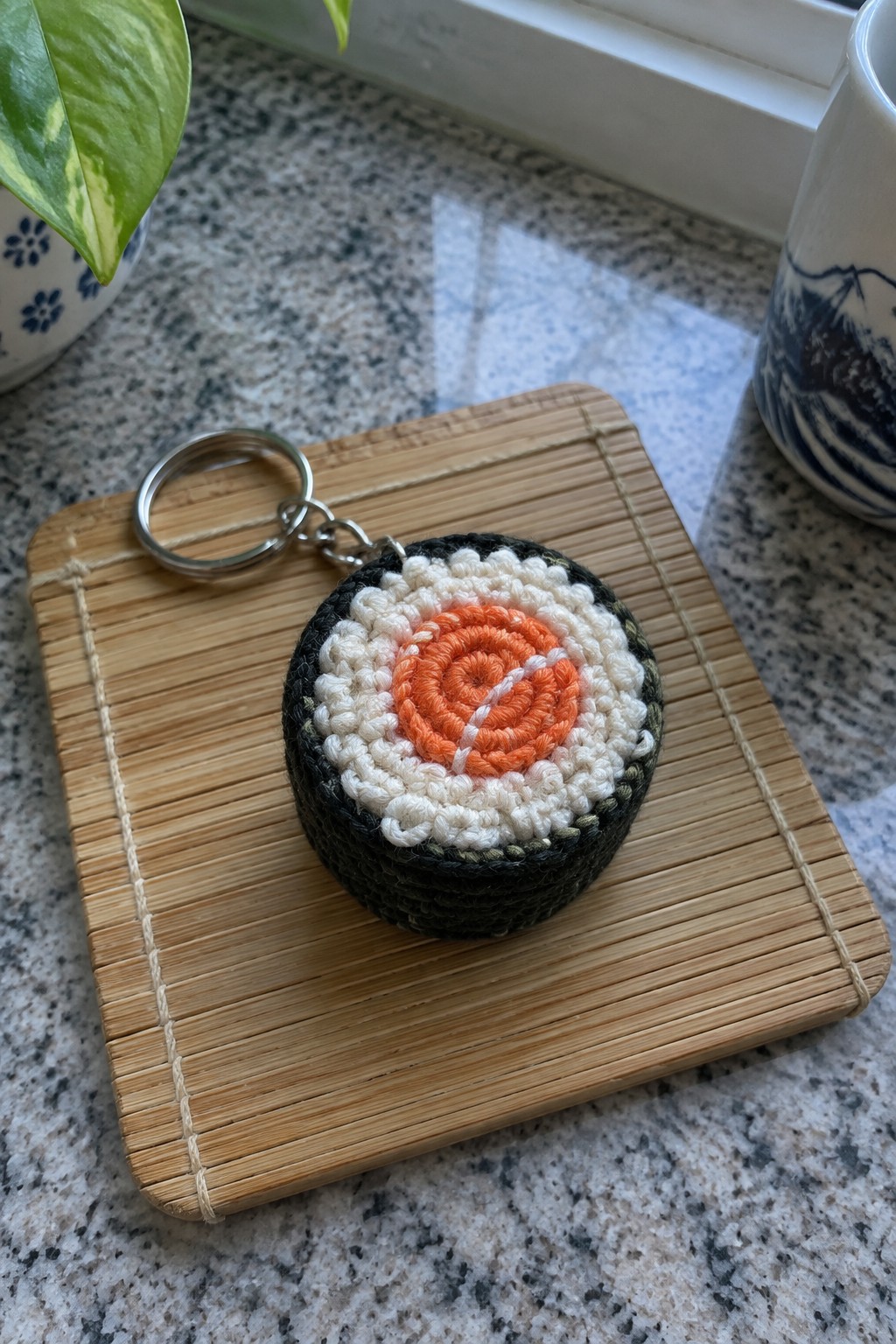 Crocheted sushi keychain with orange center on bamboo mat with keyring